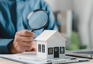 Professional agent holds magnifying, house model sits on office desk