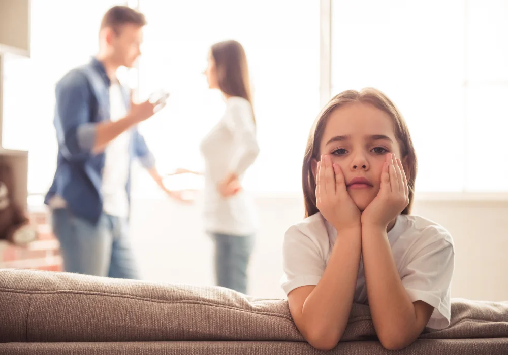 Child looking upset with adults arguing in the background