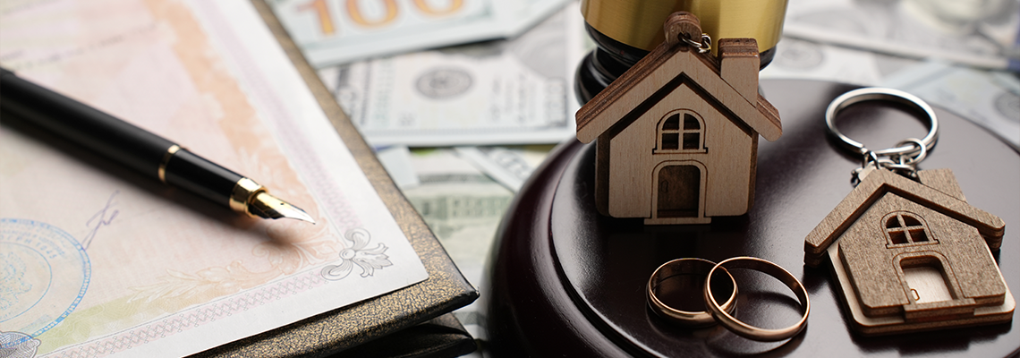 Gold wedding rings, wooden house model, and a judge gavel on legal paperwork