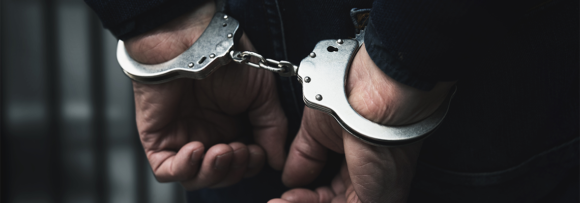 Arrested man with cuffed hands behind prison bars