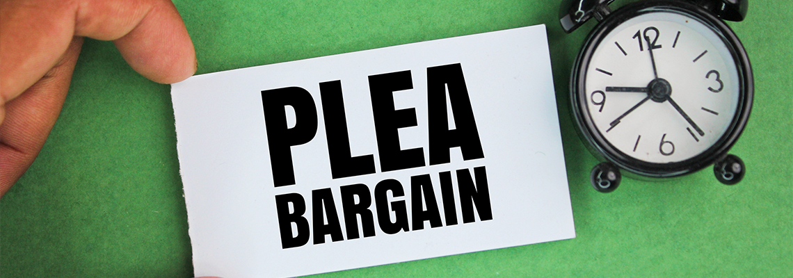 An alarm clock and a hand holding a white paper with the words plea bargain