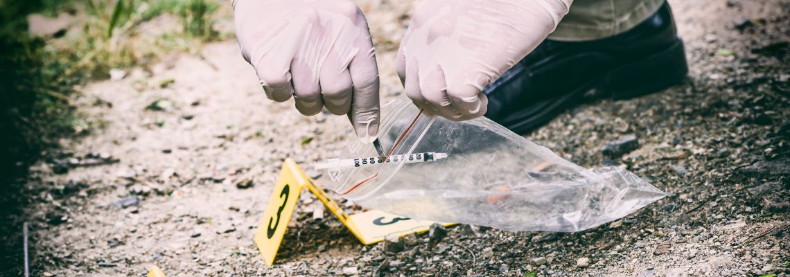 Investigators collecting drug syringe from a crime scene