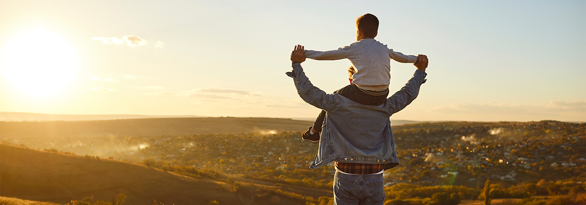 Back view of a little child boy sitting on his fathers shoulders