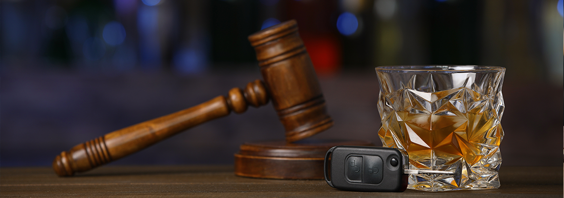 Car key, glass of alcoholic drink and gavel on wooden table in bar