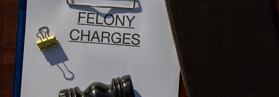 A felony charges paper secured in a clipboard, placed with a gavel