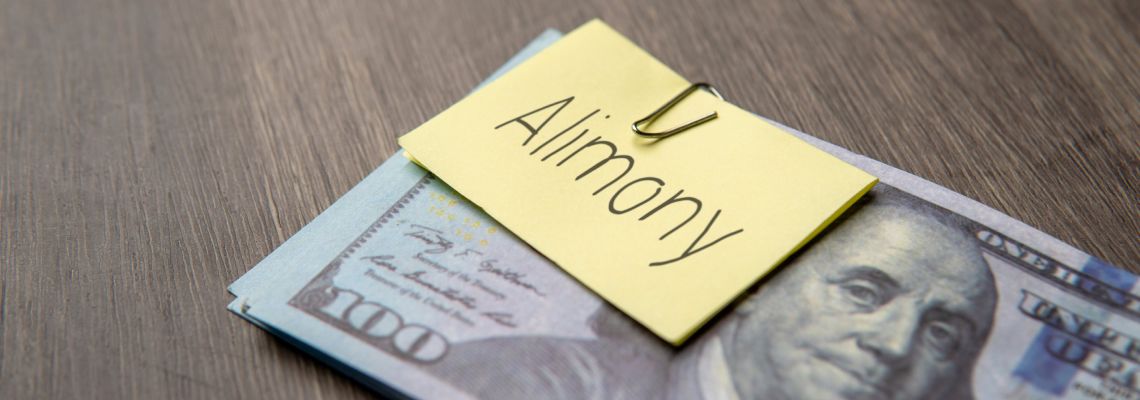 US dollar banknote clipped with a yellow note labeled alimony