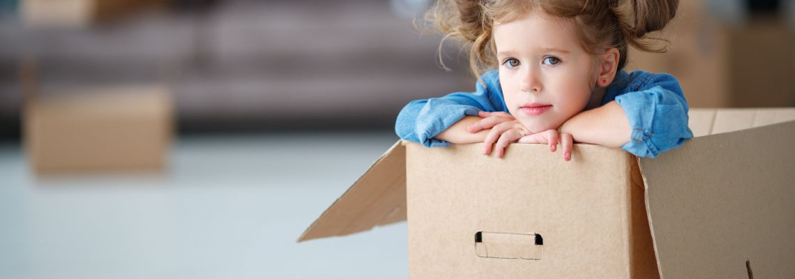 Child girl sitting in box for moving to new apartment