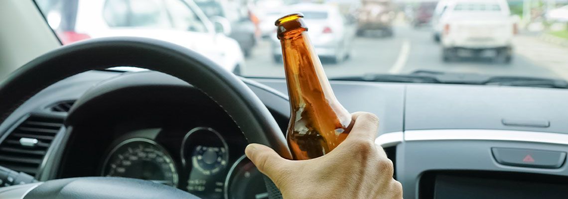 Man driving on road with beer bottle in hand