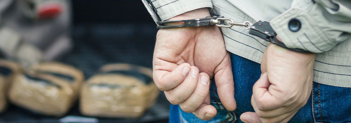 Handcuffed man with pouches of drug in background