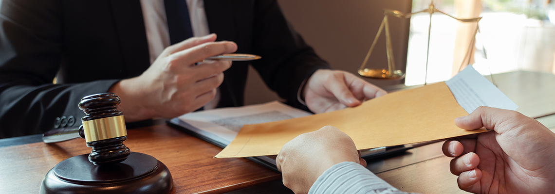 Person in suit handing paperwork to another person across desk