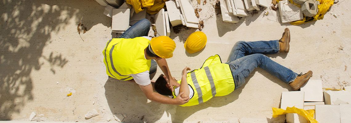 Injured construction worker on floor while co-worker tries to help