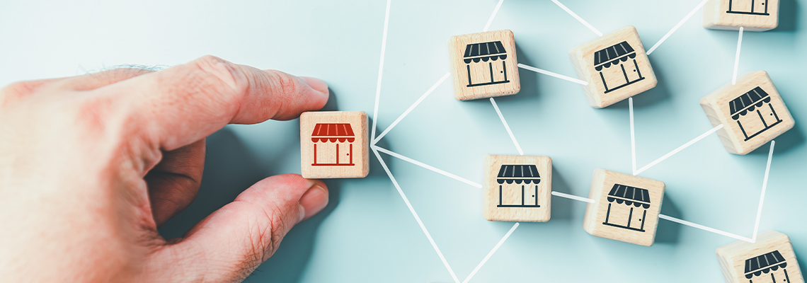 Distribution franchise branch store. Hand placing red franchising shop cube