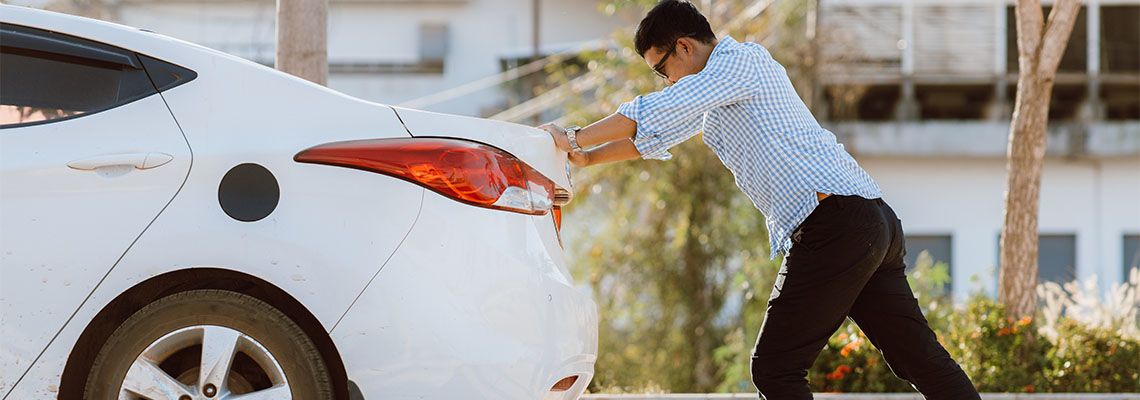 Man pushing broken car in road