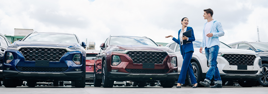 Positive female car dealership saleswoman walking along rows of new cars with customer