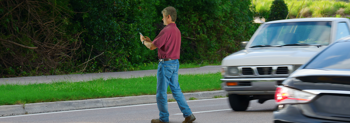 A man who is completely distracted by his cell phone is unaware that he is jaywalking