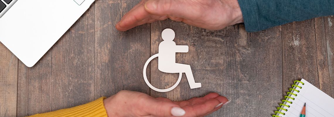 Two hands surrounding a paper cutout of the handicap symbol