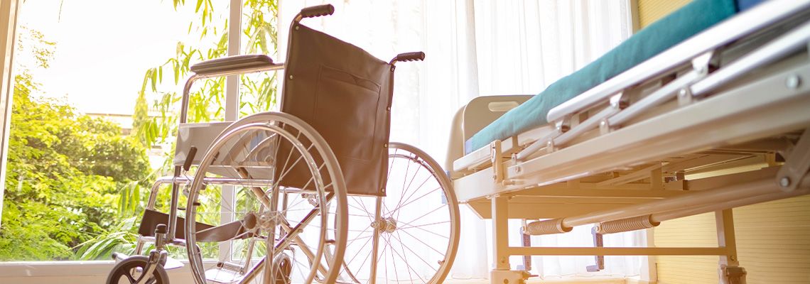 Empty wheelchair next to hospital bed in front of window