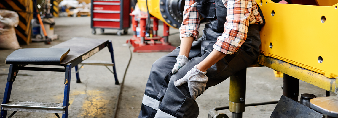 worker of warehouse in coveralls and hardhat touching hurting knee