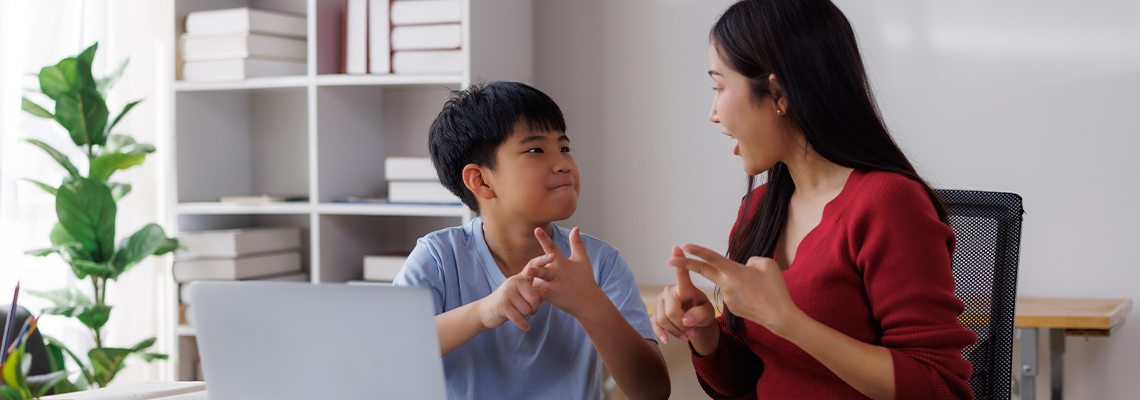Asian teacher and student communicating using sign language in classroom