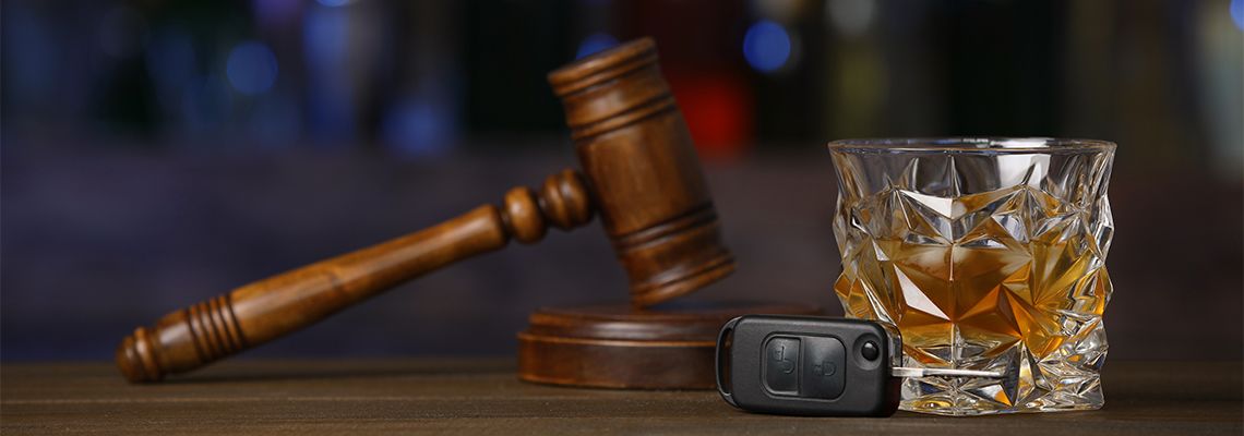 Car key, glass of alcoholic drink and gavel on wooden table