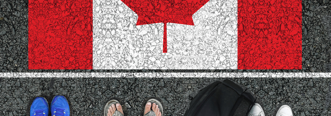 People legs is standing on asphalt road next to flag of Canada and border
