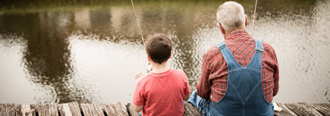 Little boy fishing with his grandpa on a dock