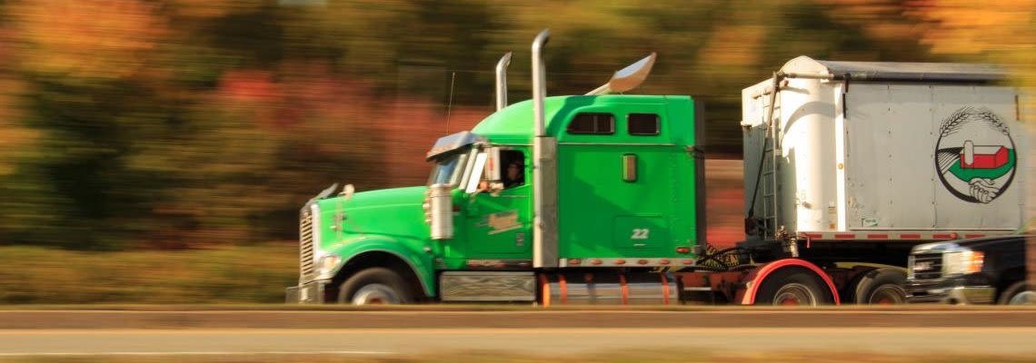 Green semi-truck driving fast down a road