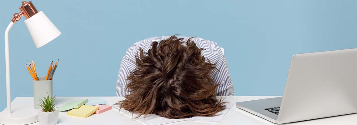 Frustrated employee lays their head down on white office desk