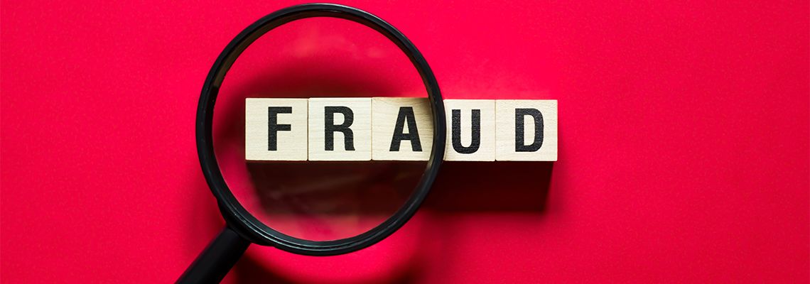 Wooden cubes forming word Fraud beneath magnifying glass