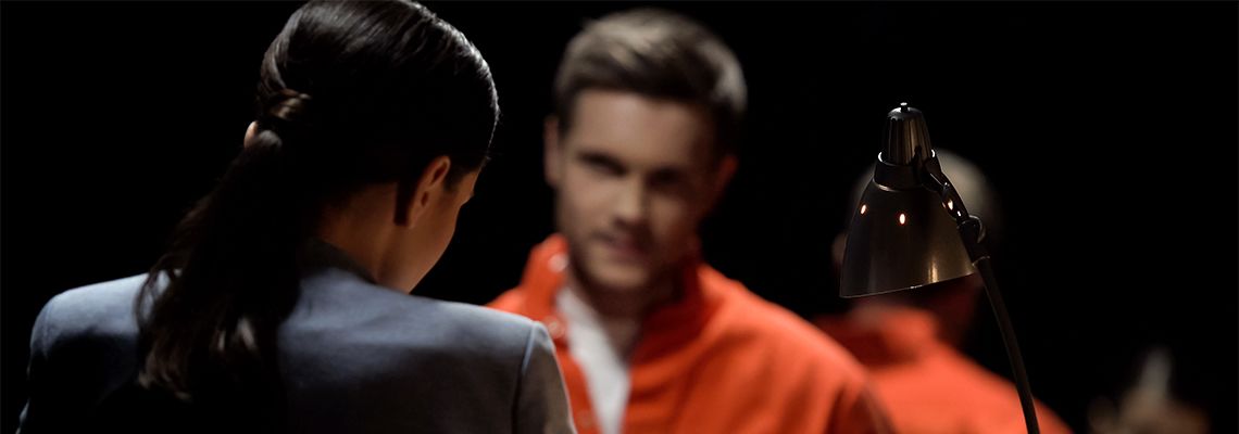 Person sitting in orange jumpsuit across from person in suit