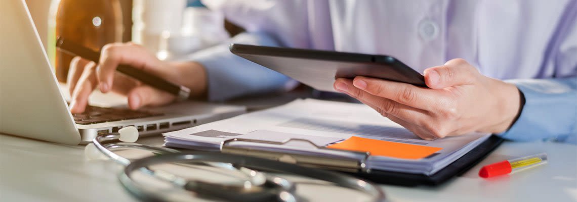 Person sitting at desk with paperwork and computer holding tablet