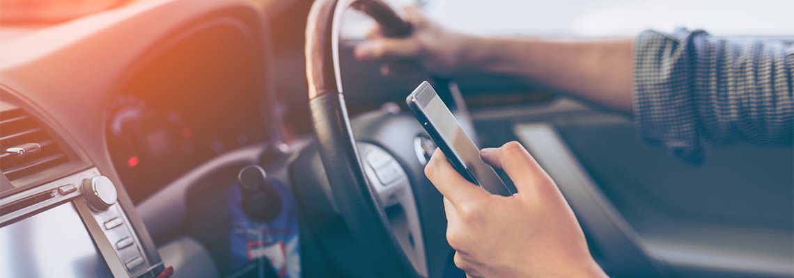 Person holding phone in hand and gripping steering wheel