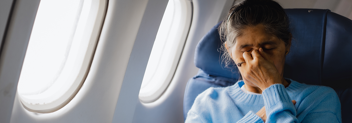 An elderly Asian woman sits inside an airplane, suffering from dizziness