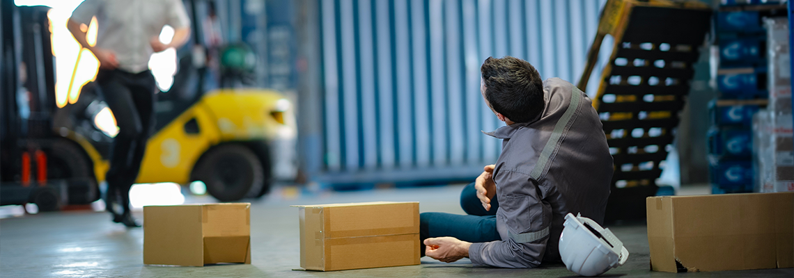 Male worker lies on ground after fall in warehouse, boxes scattered