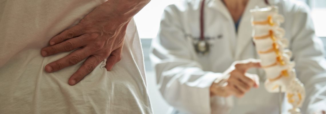 Man with back pain and doctor pointing to spine model