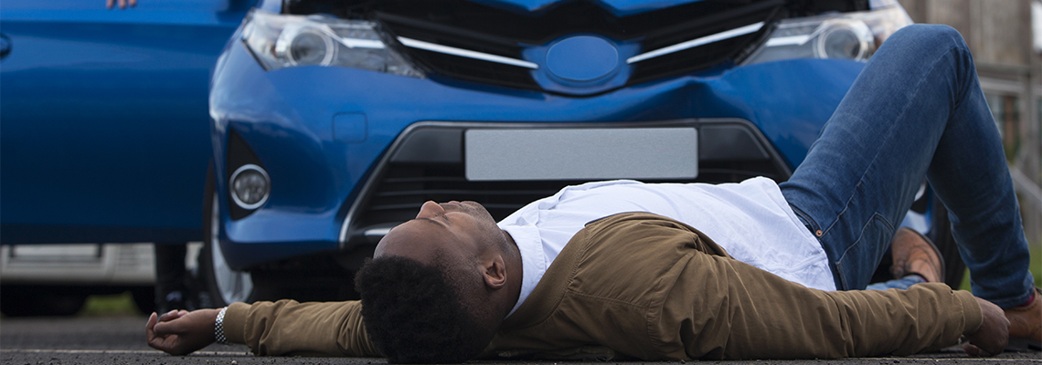 Man lays in the street in front of a car