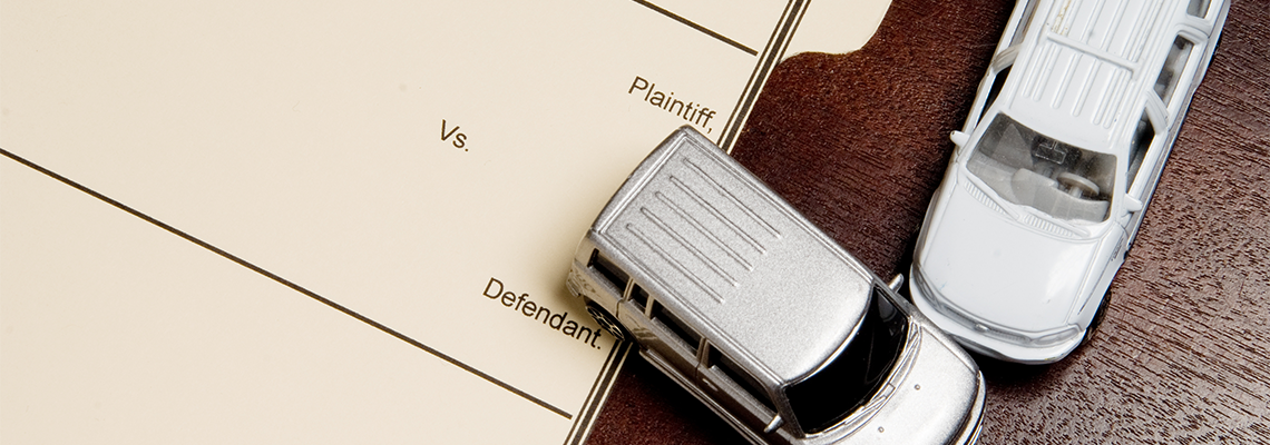 Two model cars representing car accident on paper reading plaintiff vs defendant