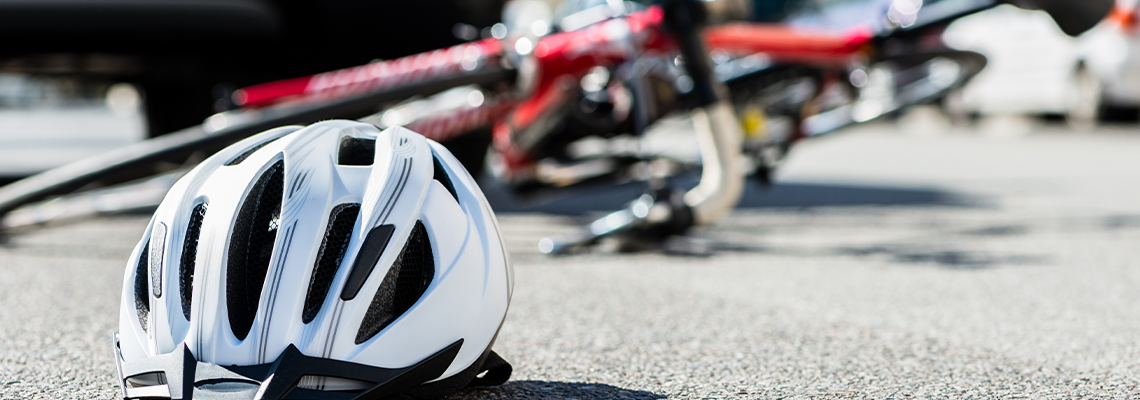 Close-up of a bicycling helmet fallen on the asphalt next to a bicycle