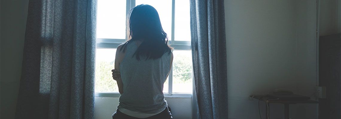 Woman sitting on bed in room with light from window