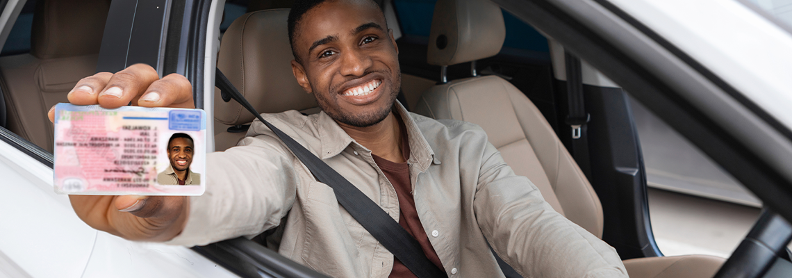 Happy young african man showing his driver's license from open car window