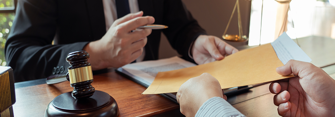 Person in suit at desk handing another person paperwork
