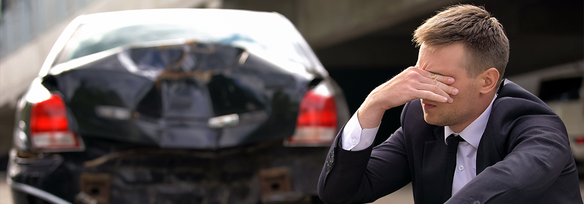 Person sitting on ground with head in hands in front of wrecked car
