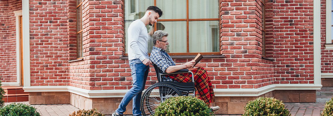 Person in wheelchair reading book while younger person pushes them