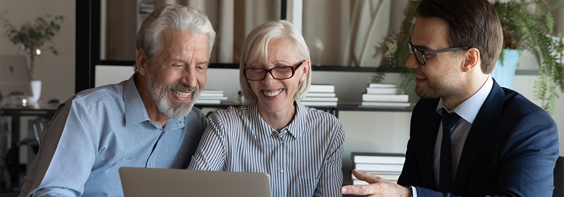 Smiling senior couple sit at lawyer broker designer office look at laptop