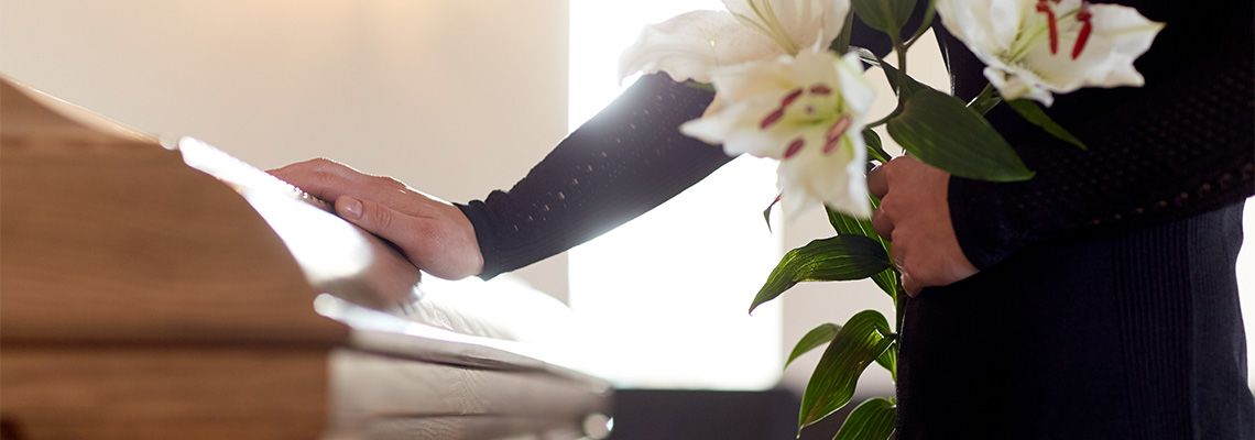 Adult holding flowers and placing hand on child's casket