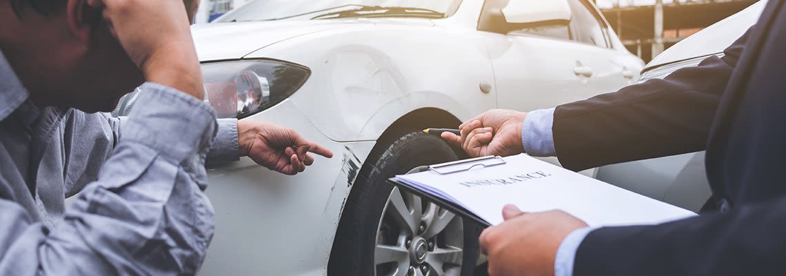 A person with a clipboard points at a damaged car