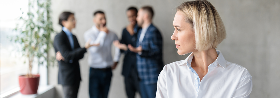 Male Coworkers Whispering Behind Back Of Unhappy Businesswoman In Office