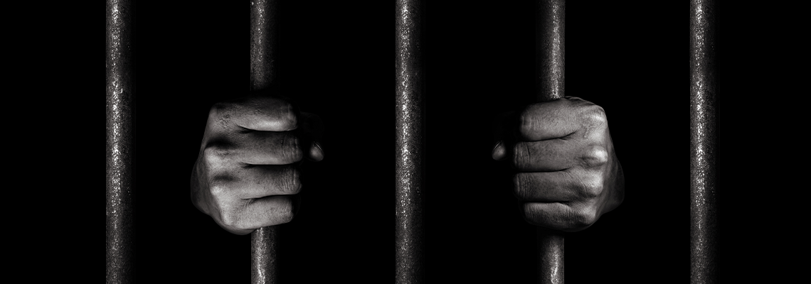 Person with hands gripping bars in jail