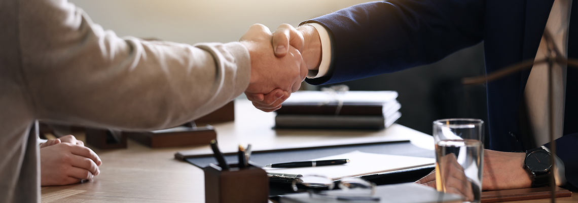 Two people shaking hands over a desk