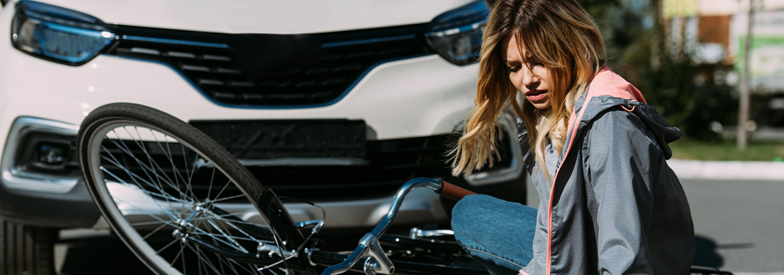 Young woman sitting in road with bike in front of vehicle